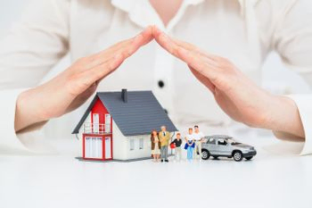 maqueta de casa con familia y coche cubierto por manos a modo de tejado